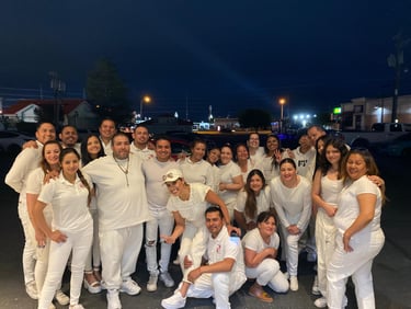 A diverse group of friends smiling and posing for a group photo outdoors at night wearing all white clothing.