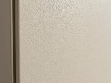 Close-up macro of PVC wall panel surface, crisp embossed grain pattern in light ivory tone, sharp panel edge visible at left, controlled studio light raking across the surface to reveal texture depth, no people