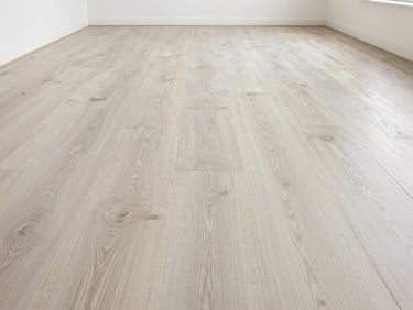 Straight-on architectural shot of vinyl plank flooring in a large empty commercial interior, light stone-effect surface, tight plank seams receding toward far wall, clean overhead diffused light, no people