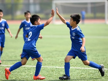 Dynamic mid-action shot of children high-fiving on a bright outdoor football pitch, sunny day, energetic blue and green tones, sharp focus, 35mm lens
