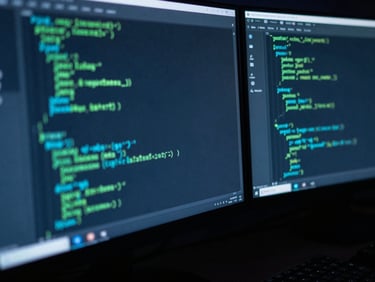 Macro close-up of a dark developer workspace, dual monitors displaying lines of clean code with subtle neon green and cyan syntax highlighting, shallow depth of field, late-night ambient screen glow.