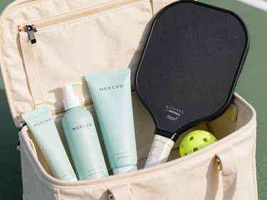 Open canvas paddle bag with MERCED Skinplus products neatly arranged inside, alongside a pickleball paddle and ball, bright outdoor lighting, clean sporty pastel tones.