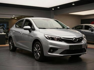 Front three-quarter view of a silver compact sedan on a clean dark showroom floor, soft overhead studio lighting, paint reflecting the ceiling lights cleanly