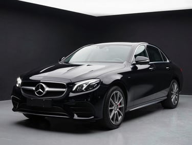 Front three-quarter angle of a black Mercedes-Benz E-Class sedan under white showroom strobe lighting, dark background, paint surface highly reflective, no people