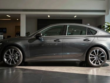 Side profile of a dark charcoal mid-size sedan on a polished showroom floor, dramatic side lighting casting a sharp highlight line along the door panels