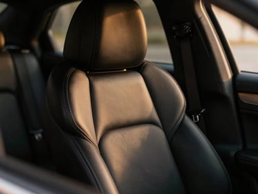 Macro shot of hand-stitched black leather seats inside a luxury sedan, soft ambient gold lighting, pristine interior, 35mm