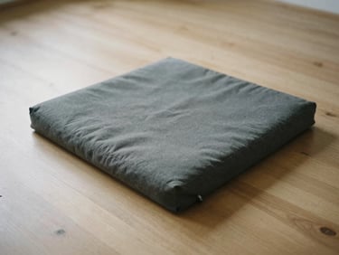 An empty dark grey meditation cushion on a light wooden floor, soft morning light, minimalist film photography, muted earthy tones, quiet contemplative mood, 35mm