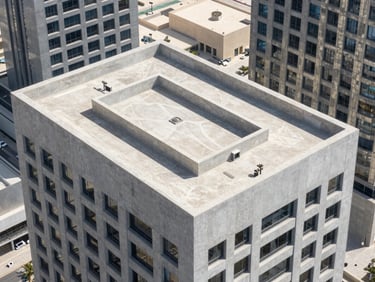 High-angle architectural shot of a modern skyscraper roof in Dubai, clean gray concrete, sharp shadows under bright desert daylight.