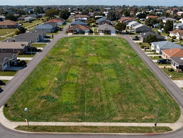 Raw land parcel, wide environmental framing showing lot boundaries and adjacent properties, natural daylight, clear sight lines, zoning markers visible in context, no people or staging