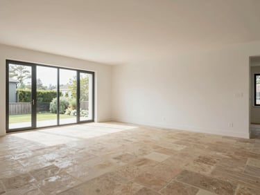 Wide-angle view of a completed luxury residential living room interior, warm stone flooring, clean white walls, natural north-facing daylight, empty room showing spatial proportions, no people
