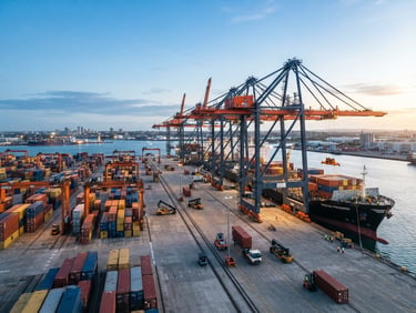 Wide-angle industrial editorial shot of a modern cargo terminal at dawn, crisp morning daylight, high-contrast cool tones with subtle orange crane accents, sharp focus, 35mm