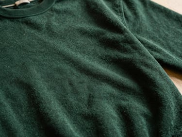 Close-up of a heavy cotton sweatshirt fabric, deep forest green, with subtle texture visible under warm, dramatic side-lighting, shallow depth of field.
