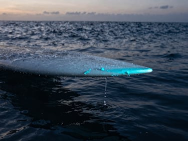Macro detail of a surfboard rail with water dripping, electric cyan wax, high-contrast dawn light, deep blue water in background