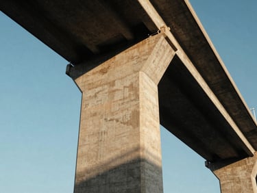 Low-angle monumental shot of a massive finished concrete highway bridge pier stretching into the sky, sharp architectural shadows, high-contrast, golden hour