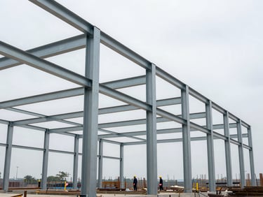 Wide-angle view of a bolted steel frame structure mid-assembly on a construction site, overcast daylight, workers in hard hats visible at lower frame, structural columns and cross-bracing clearly legible