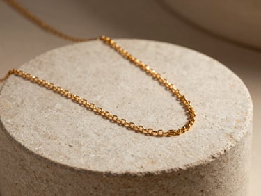 Elegant close-up of a gold necklace draped over a textured stone pedestal, warm directional studio lighting