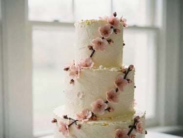 A beautifully decorated multi-tier celebration cake with delicate sugar cherry blossoms, soft natural window light, muted pastel tones, shallow depth of field, 35mm.