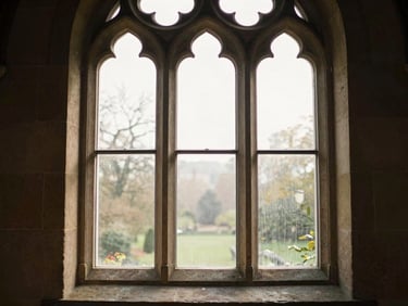Quiet environmental shot of a historical stone church window with soft morning light streaming through, 35mm