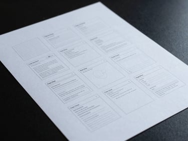 Crisp UI wireframes printed on stark white paper under cool studio lighting, sharp shadows.