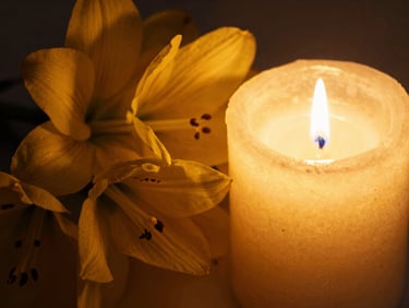 Extreme close-up of fresh yellow flowers resting beside a burning golden candle, soft shadows, warm amber lighting, 35mm