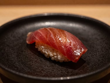 Close-up of glistening tuna nigiri on a matte black ceramic dish, warm side-lighting, shallow depth of field.