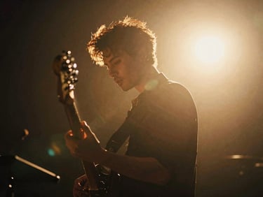 Cinematic film photography of a musician under dramatic backlighting, rich golden-hour natural light, anamorphic lens flare, shallow depth of field.