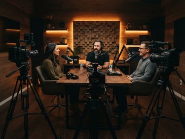 Cinematic wide shot of a podcast studio with three high-end cameras on rigs, soft amber backlighting, acoustic wood paneling, shallow depth of field.