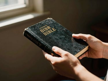 Hands holding a Bible inside a dimly lit room, soft light streaming from a window, peaceful atmosphere, 35mm