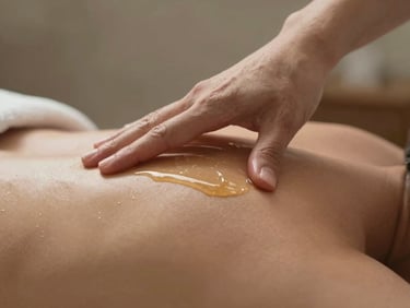 Extreme close-up of warm massage oil being applied to a client's shoulder, therapist thumb pressing into the trapezius, diffused studio light, soft earth-tone background