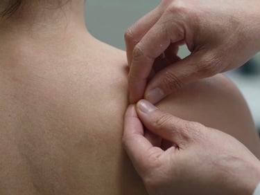 Extreme close-up of therapist thumb working into a dense knot on a client's upper trapezius, high-contrast soft light from above, skin texture and pressure point clearly visible