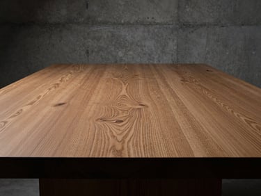 Close-up of a cured Friuli oak tabletop, showing rich grain and texture, dramatic side-lighting, brutalist concrete background.