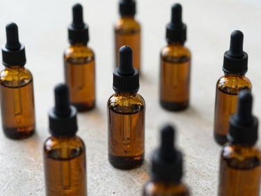 Macro close-up of amber glass dropper bottles filled with botanical tinctures, with dried herbs and compounding tools on a light stone surface, soft natural daylight, 35mm lens