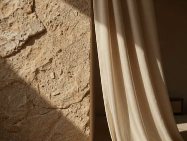 Extreme close-up of raw textured stone wall meeting soft silk drapery inside a minimal desert pavilion, warm low-key natural light casting long shadows.