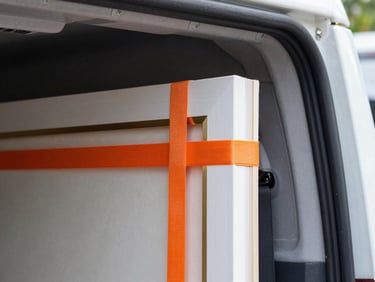 Close-up of secure orange strapping holding a wrapped fine art frame inside a transport vehicle, precise tension, sharp focus