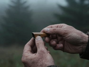 Tight macro shot of a weathered hand tuning a wooden duck call, low-light dawn, moody desaturated tones.