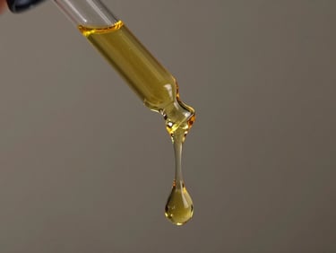 Close-up of a single golden drop of pure botanical oil dripping from a glass pipette, captured in slow motion.