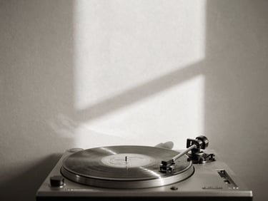 Minimalist black and white photography of a single vinyl record spinning on a turntable, soft natural window light casting long shadows on a cream plaster wall, sepia undertones