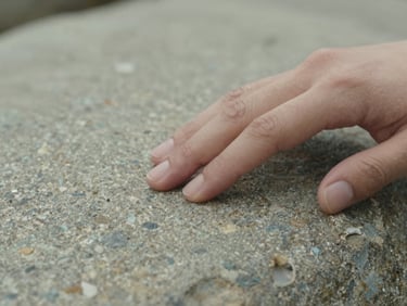 Close-up of a hand gently touching a smooth, textured stone, soft natural light, focus on texture and calm
