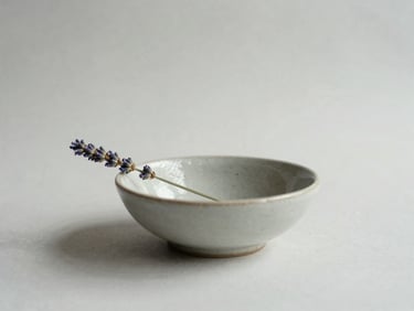 Minimalist still life with a ceramic bowl and a single sprig of dried lavender, soft diffused light, serene and elegant