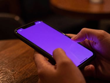 Extreme close-up of hands holding a glowing smartphone in a moody low-light cafe, vibrant purple screen-glow reflecting on fingers, 35mm photography