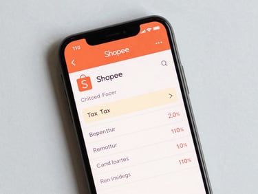 Close-up overhead flat-lay of a smartphone screen showing the Shopee checkout page with a tax line item highlighted, on a clean white surface, studio daylight, no shadows