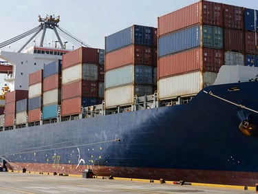 A cargo container ship docked at a modern port terminal, with large metal shipping containers being organized in daylight.