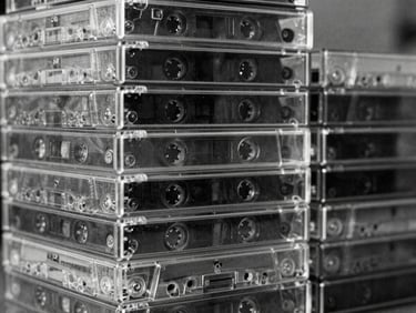 Close-up stack of unlabelled cassette tapes in clear plastic cases, raw analog grain, high contrast monochrome, 35mm film photography