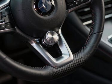 Close-up of a premium machined metal steering wheel dial and carbon fiber console trim, high-contrast studio lighting, moody shadows.