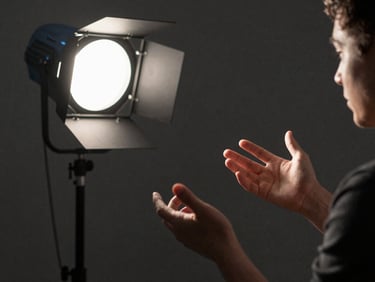Documentary film still, a documentary subject's hands gesturing mid-interview, side-lit by a single practical lamp against a dark wall, film grain texture, shallow depth of field, charcoal tones