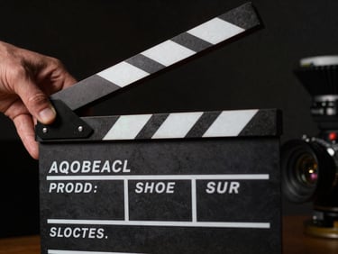 Close-up of a film clapperboard snapping shut on a dark studio set, dramatic side-lighting, film grain texture, hands partially visible, deep shadows