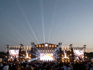 Dramatic wide angle of a massive festival stage with linear arrays, laser beams, and a crowd silhouette.