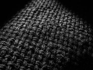Extreme close-up of heavy black cotton fabric weave, high-contrast directional light creating sharp shadows, minimalist studio setting, 35mm