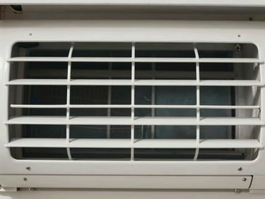 Close-up of a clean white air conditioning vent grille, shot directly from the front in flat natural daylight, fins and mesh detail sharp and clearly visible, no people, no chemicals