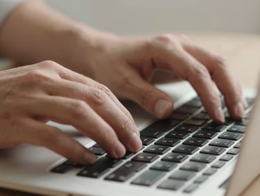 Extreme close-up of hands typing a tracking number into a laptop keyboard, neutral studio light from above, only fingertips and keys in frame, mid-task feel, no warmth or staging